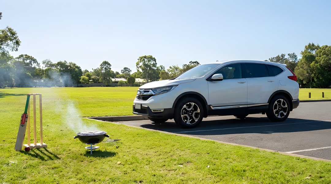 White SUV parked near a grassy park with BBQ and cricket gear. No people. Sunny day