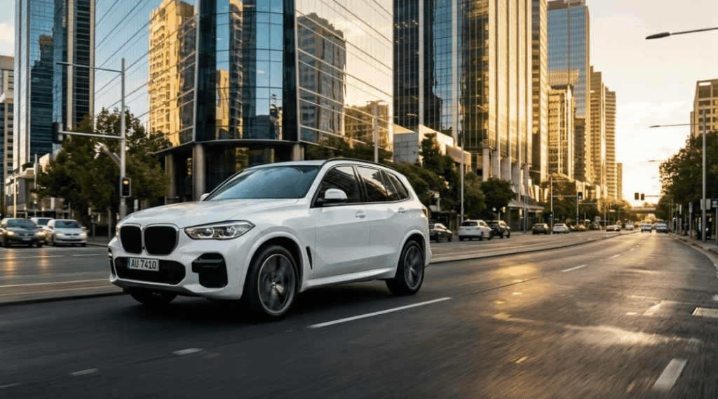 modern white SUV driving smoothly on a sealed asphalt road through a sunlit, modern city street. Tall skyscrapers with sleek glass facades reflect the warm, golden hour sunlight