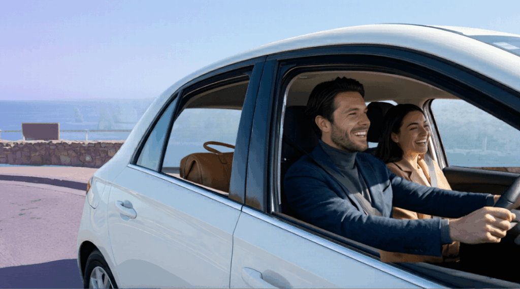 Our stylish couple enjoying a stunning panoramic view of the iconic Great Ocean Road Twelve Apostles formations from inside their clean, white rental compact hatchback.