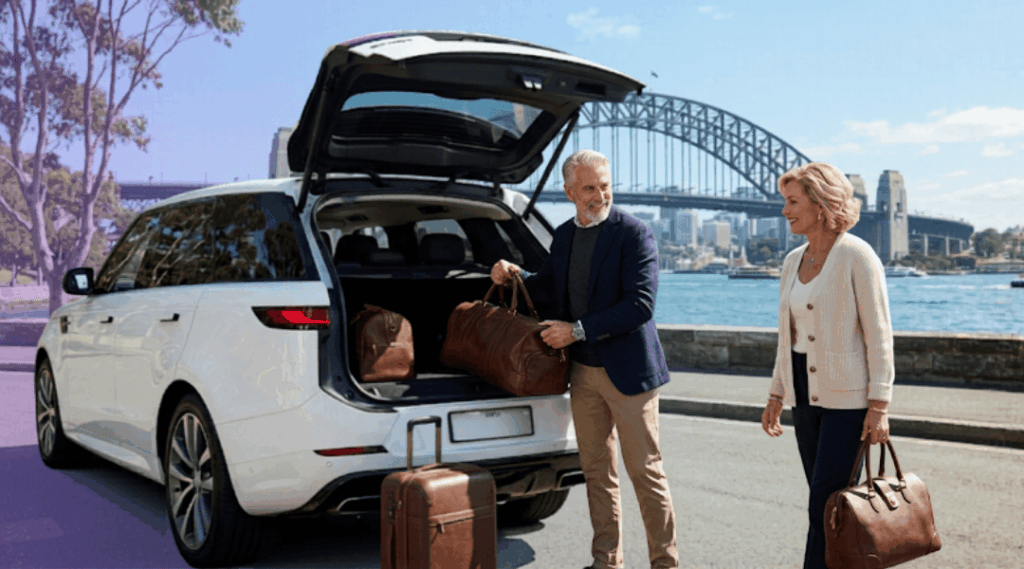 Our sophisticated silver fox couple loading high-end leather travel gear into their white luxury SUV from our Sydney City branch, with a clear view of the iconic Sydney Harbour Bridge and city skyline across the water under a clear, bright midday sun.